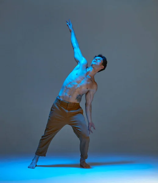 スタジオでネオンライトでシャツなしで表現力豊かなダンスを踊るクールな若い男。ダンススクールのポスター。タトゥーのある体 — ストック写真