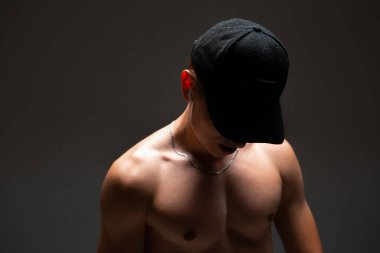 Şapkalı ve kablosuz kulaklıklı havalı genç adam siyah arka planda tişörtsüz şarkı dinliyor. Müzik posteri