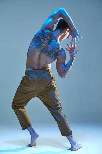 Giovane fresco in danza espressiva senza camicia in luce al neon. Manifesto della scuola di danza. Corpo con tatuaggi. Vista da dietro — Foto Stock