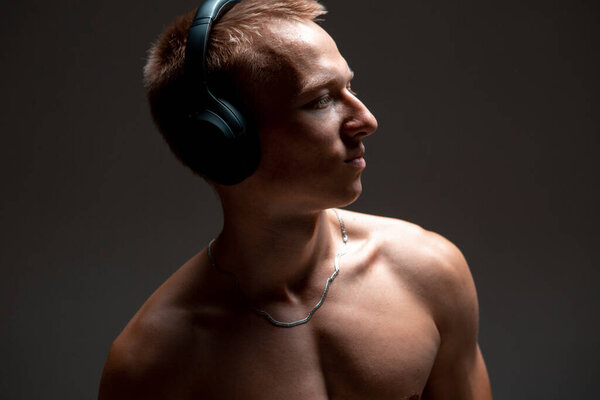 Cool young guy in wireless headphones listen to song with naked torso in studio. Music poster. High quality photo