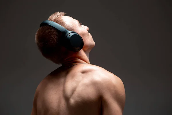 Menő fiatal srác vezeték nélküli fejhallgatóval zenét hallgat meztelen felsőtesttel a stúdióban. Zenei poszter — Stock Fotó