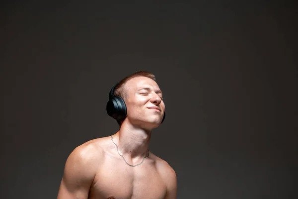 Menő, fiatal, mosolygós srác vezeték nélküli fejhallgatóval, aki meztelen felsőtestes dalt hallgat a stúdióban. Zenei poszter — Stock Fotó