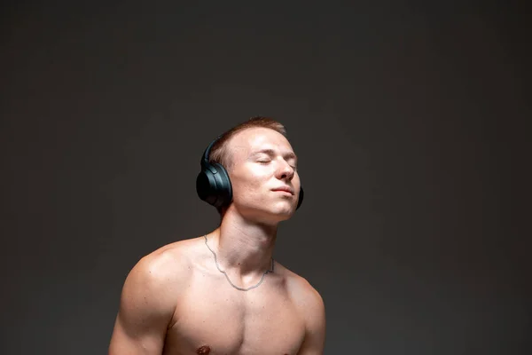 Cool joven bailarín en auriculares inalámbricos escuchar canciones y bailar hip-hop sin camisa. Cartel de música y danza —  Fotos de Stock