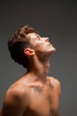 Stüdyoda tişörtsüz, şık saç kesimi olan yakışıklı bir gencin portresi. Dövmeli vücut.