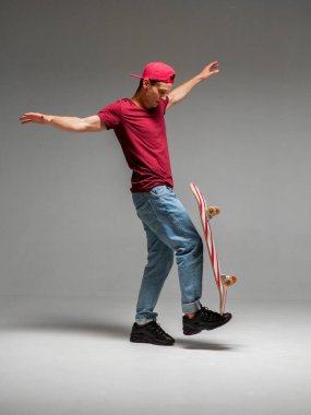 Havalı kaykaycı stüdyoda kaykayı gri arka planda tutuyor. Kaykay ve denge hakkında fotoğrafçılık