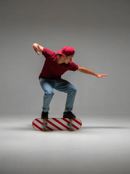 Cool guy skateboarder stands on skateboard in studio on grey background. Photography about skateboarding and balance