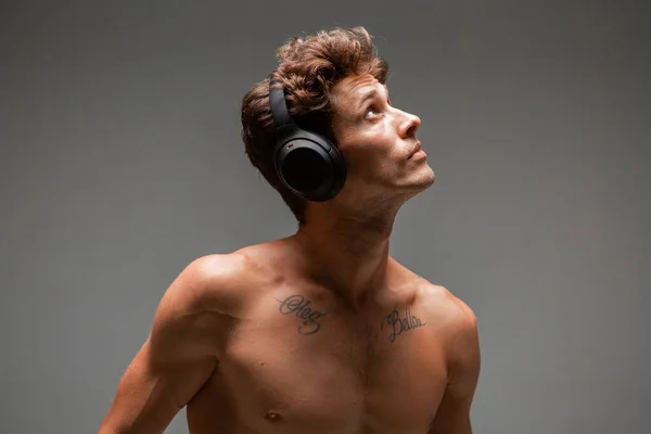 Portrait de jeune homme élégant dans un casque sans fil écoutant des chansons avec des épaules nues en studio. Affiche musicale — Photo