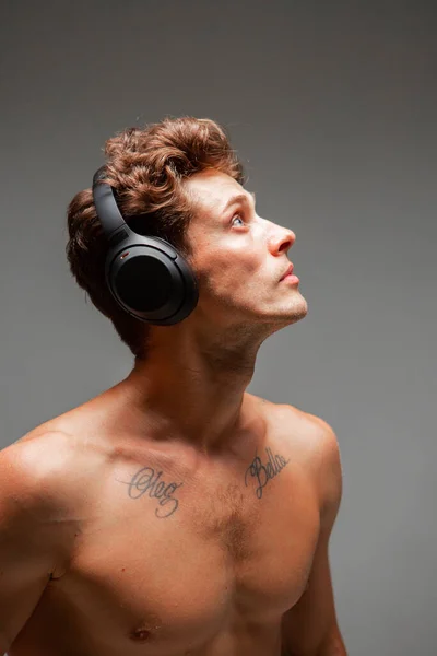 Stílusos fiatalember vezeték nélküli fejhallgatóval, aki meztelen vállakkal hallgatja a dalt a stúdióban. Zenei poszter — Stock Fotó