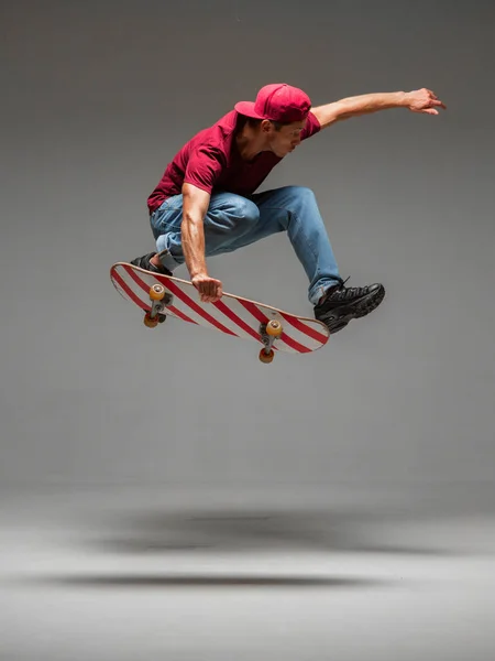 Cool jeune homme skateboarder saute sur skateboard en studio sur fond gris. Photographie sur les tours de skateboard — Photo