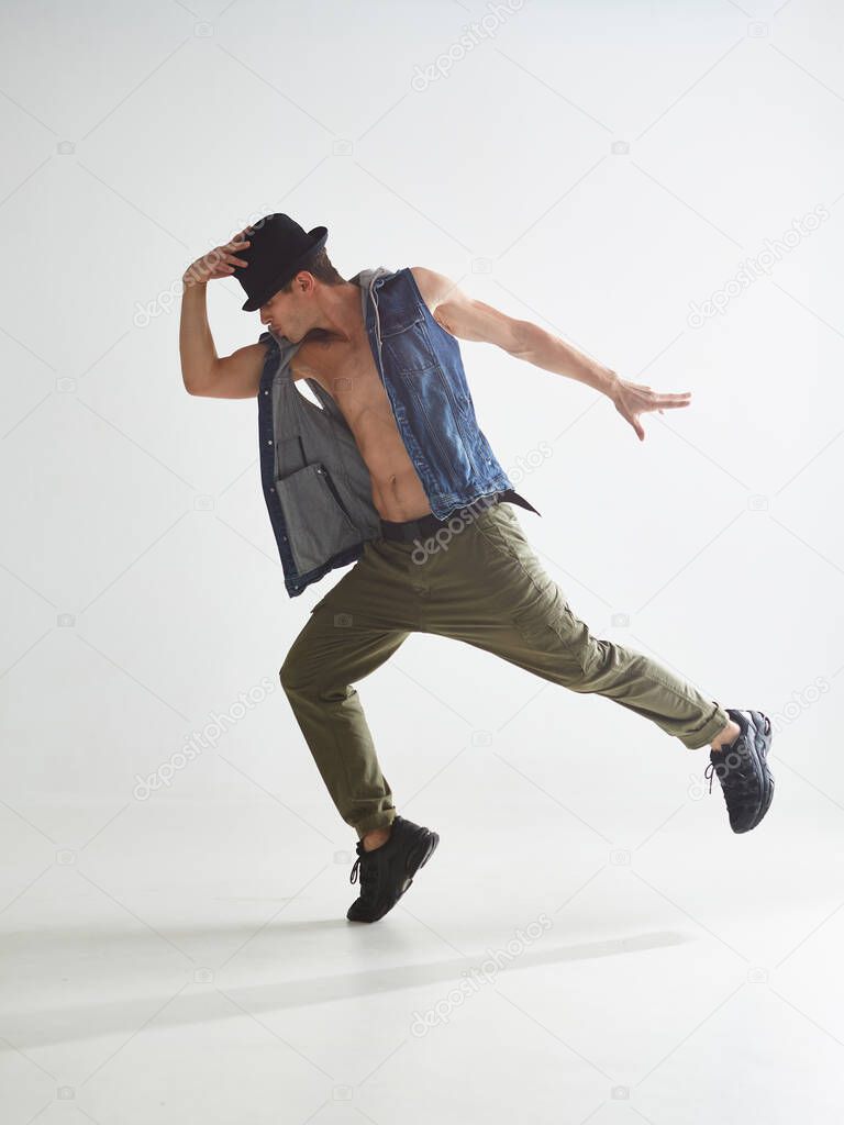 Cool young guy breakdancer in hat dancing hip-hop in studio isolated on white background. Break dance lessons