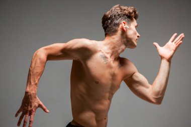 Kablosuz kulaklıklı genç seksi adam. Gri arka planda çalışan çıplak gövdeli bir şarkı dinliyor. Dövmeli güzel bir vücut.