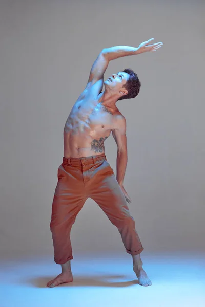 スタジオでネオンの光の中でシャツなしで踊るクールな若い男のダンサー。ダンススクールのポスター。タトゥーのある体 — ストック写真