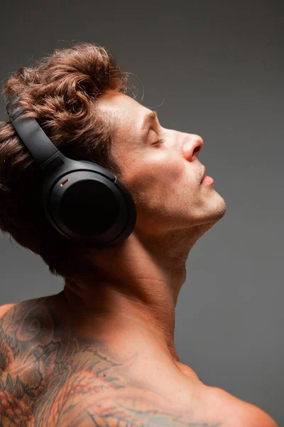 Portré elegáns fiatalember vezeték nélküli fejhallgató hallgat dalt meztelen törzs a stúdióban. Zenei poszter — Stock Fotó