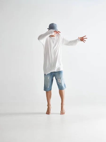 Elegante giovane breakdancer ragazzo in cappuccio che copre il viso con le mani si erge in punta di piedi scalzi in studio su sfondo bianco — Foto Stock
