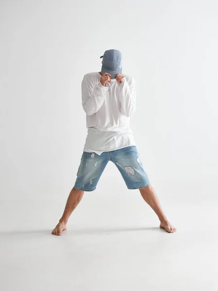 Cool breakdancer ragazzo a piedi nudi in piedi in studio che copre il viso con un tappo isolato su sfondo bianco — Foto Stock