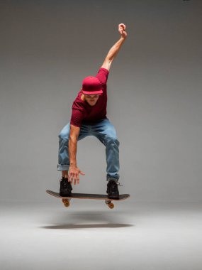Havalı genç kaykaycı gri arka planda stüdyoda kaykayla havada süzülüyor. Kaykay numaraları hakkında fotoğrafçılık