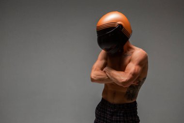 Kasklı, çıplak gövdeli atletizm yarışçısı stüdyoda gri arka planda duruyor. Kart yarış posteri. Dövmeli vücut.
