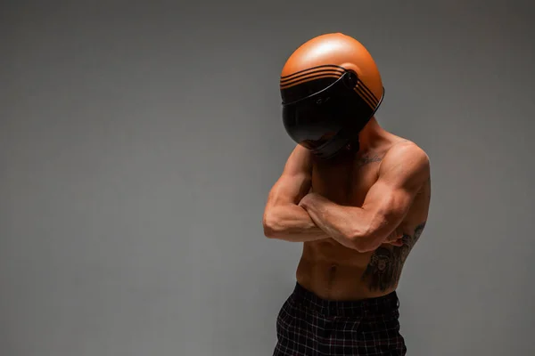 Atletico ragazzo corridore in casco con busto nudo si erge su sfondo grigio in studio. Manifesto gara kart. Corpo con tatuaggio — Foto Stock
