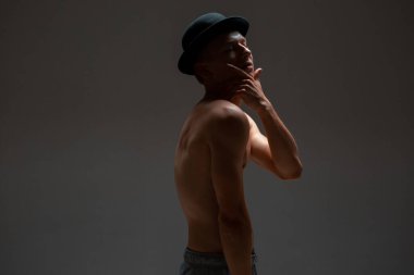 Stüdyoda siyah arka planda tişörtsüz şık bir genç oyuncu.