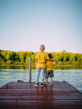 Havalı çocuklar birbirlerine sarılır ve rıhtımda kalan nehre bakarlar. Arka plan