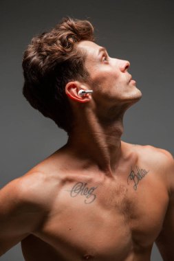 Kablosuz kulaklıklı havalı genç adam çıplak gövdesiyle şarkı dinliyor. Müzik posteri. Dövmeli vücut.