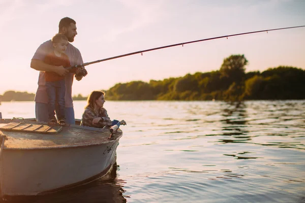 Joven pesca familiar en barco en el río en verano. Padre enseña a pescar. Foto para blog sobre viajes en familia —  Fotos de Stock