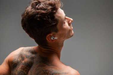 Kablosuz kulaklıklı havalı genç adam tişörtsüz şarkı dinliyor. Müzik posteri. Dövmeli vücut..