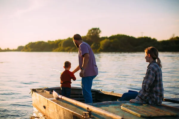 Young family fishing on boat on river in summertime. Back view. Photography for ad or blog about family and travel