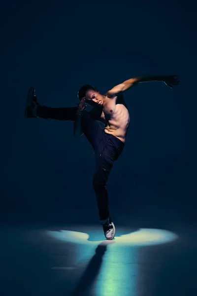 Młody facet tancerz z nagim tułowiem tańczący w studio w świetle reflektorów na czarnym tle. Plakat szkoły tańca — Zdjęcie stockowe