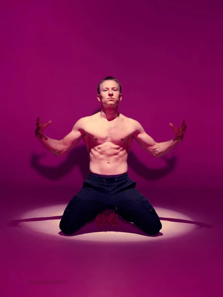 Cool ung kille dansare med naken torso dansar i studio på knä i rosa ljus i rampljuset. Affisch för dansskolan — Stockfoto