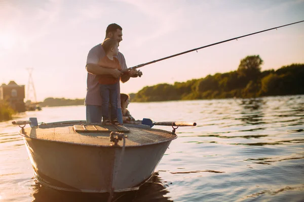 Joven pesca familiar en barco en el río en verano. Padre enseña a pescar. Foto para blog sobre viajes en familia —  Fotos de Stock