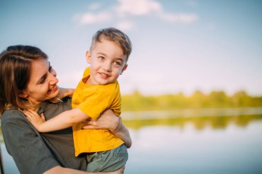 Anne ve oğul rıhtımda otururken birbirlerine sarılıyorlar. Aile ve seyahat hakkında bir blog ya da reklam için yaz fotoğrafçılığı