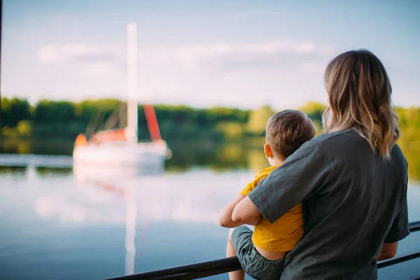 Young mother with cool kid boy stand on dock, look at sailboat. Back view. Summer photography about family and travel