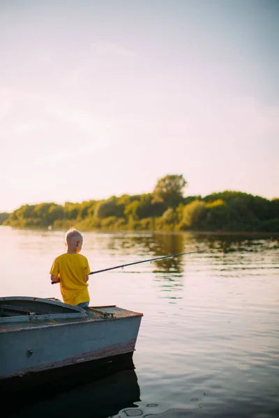 Elegante bebé pescador niño con una caña de pescar en la mano de pesca desde el barco en el río en verano —  Fotos de Stock