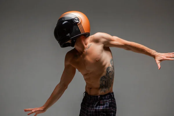 Cool gars coureur dans le casque avec torse nu se tient sur fond gris en studio. Affiche de course Kart. Corps avec tatouage — Photo