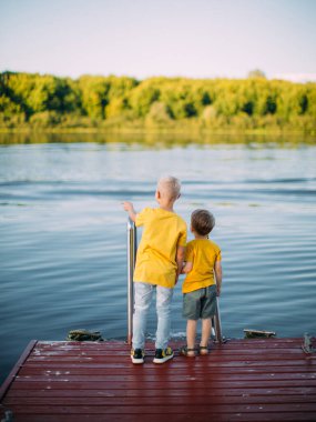Havalı erkek kardeşler rıhtımda kalıp el ele tutuşup nehri seyrediyorlar. Arka plan