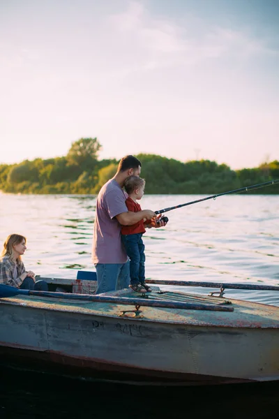 Young family fishing on boat on river in summertime. Father teaches son fishing. Photo for blog about family travel