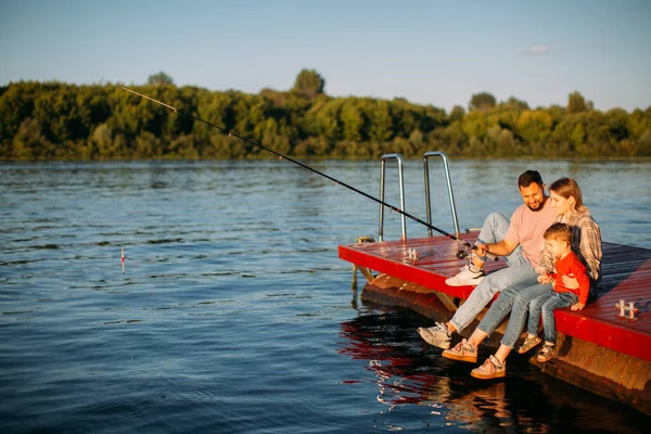 Feliz joven familia de pesca en el muelle en el río o lago en verano. Fotografía para anuncio o blog sobre familia y viajes —  Fotos de Stock