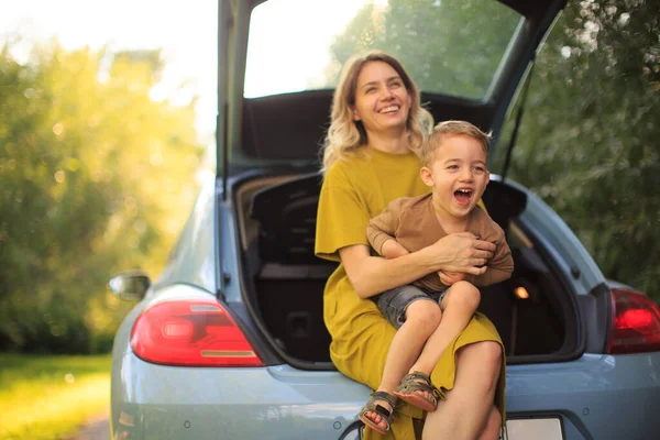 Güzel anne ve küçük oğul gezginler bir arabanın bagajında oturup gülüyorlar. Aile seyahati hakkında fotoğraf