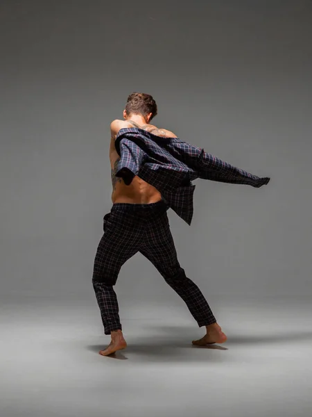 Stylowy młody facet tancerz tańczący w garniturze boso odizolowany na szarym tle. Widok z tyłu. Plakat szkoły tańca — Zdjęcie stockowe