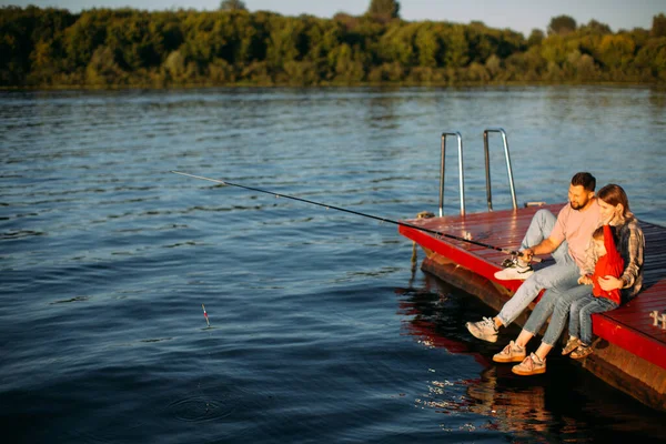 Feliz pesca familiar en el muelle en el río o lago en verano. Fotografía para anuncio o blog sobre familia y viajes —  Fotos de Stock