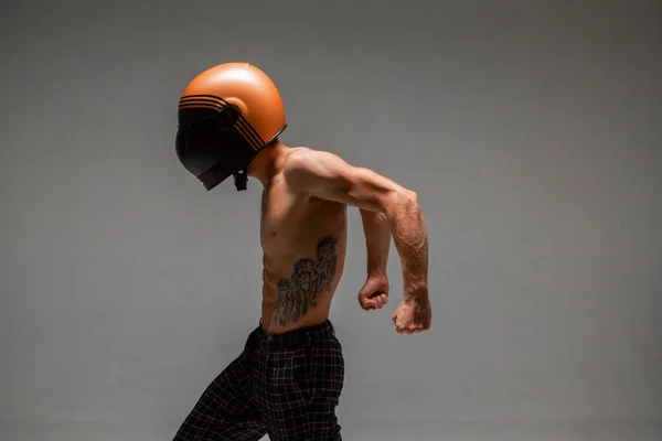 Ragazzo fresco corridore in casco con busto nudo si erge su sfondo grigio in studio. Manifesto gara kart. Corpo con tatuaggio — Foto Stock