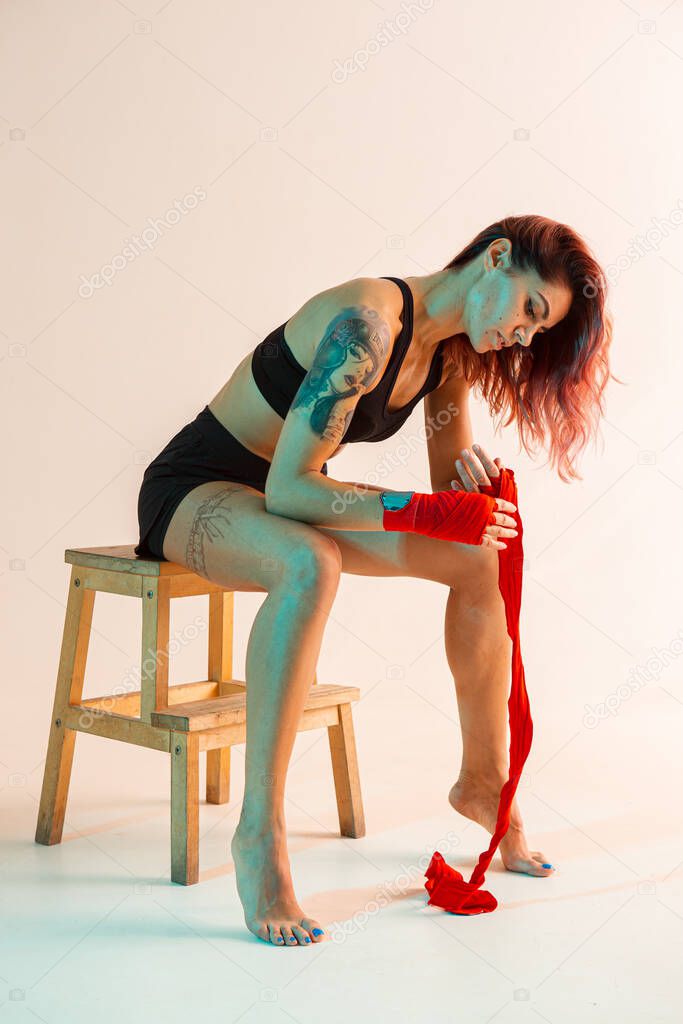 Beautiful female fighter putting on boxing bandages in studio in neon light. Mixed martial arts poster