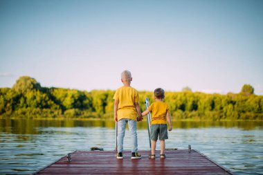 Havalı çocuklar el ele tutuşup rıhtımda kalan nehre bakarlar. Arka plan