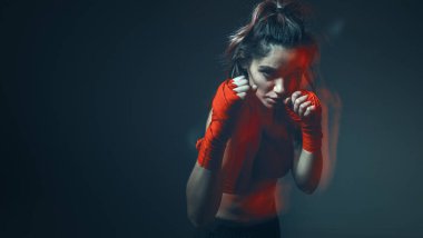 Güzel kadın dövüşçü boks bandajlarıyla gri arka plandaki stüdyoda antrenman yapıyor. Kadınların karma dövüş sanatları posteri.