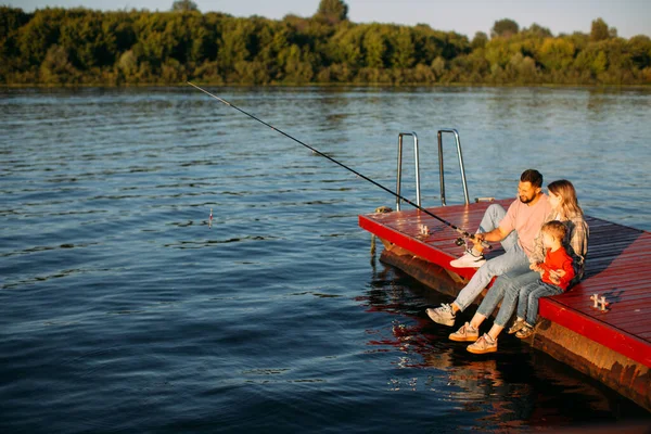 Joven pesca familiar en el muelle en el río o lago en verano. Fotografía para anuncio o blog sobre familia y viajes —  Fotos de Stock