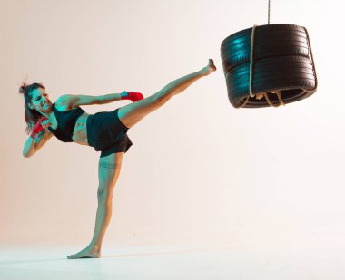 Tekme pratiği yapan kadın boksör stüdyoda lastik kullanıyor neon rengi arka planda izole edilmiş. Karışık dövüş sanatları posteri