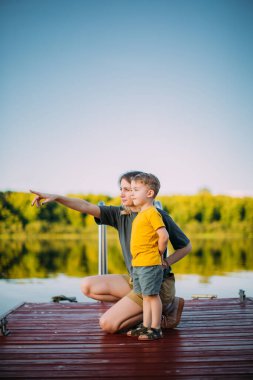 Havalı bir oğlan ve annesi iskelede durmuş nehri seyrediyorlar. Blog için yaz fotoğrafçılığı ya da aile ve seyahat hakkında reklam