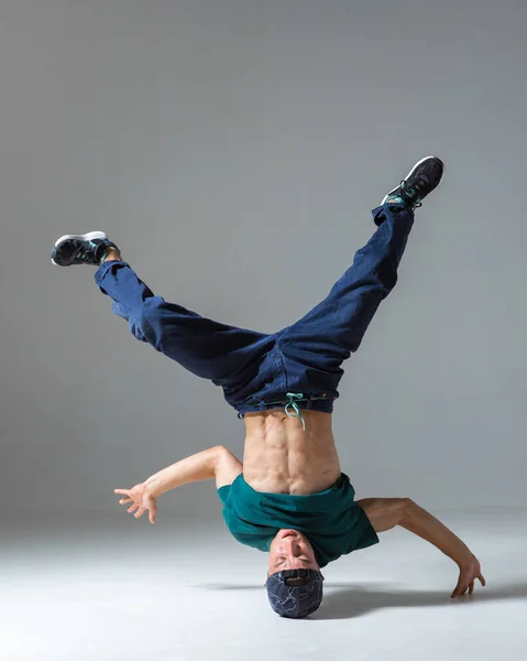 Stylowy facet tancerz taniec na head breakdance w studio odizolowany na szarym tle. Lekcje przerwy — Zdjęcie stockowe