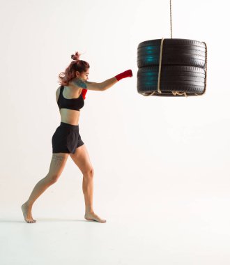 Lastiklerden yapılmış kum torbasıyla boks yapan atletik kız boksör kız, beyaz arka planda izole edilmiş. Karışık dövüş sanatları posteri